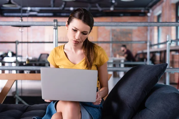 Dissatisfied businesswoman using laptop while sitting on sofa in office — Stock Photo