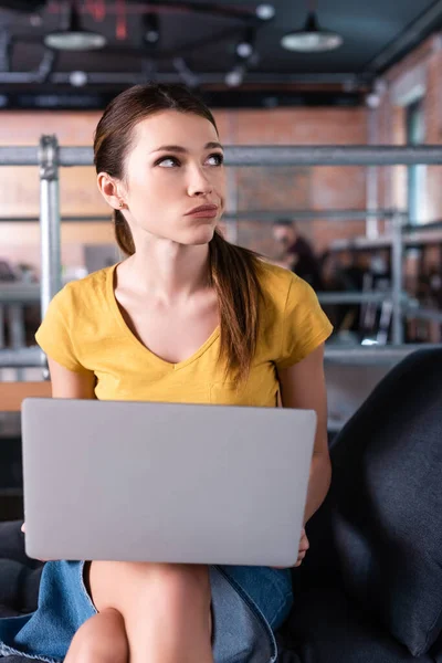 Dissatisfied businesswoman using laptop and looking away in office — Stock Photo