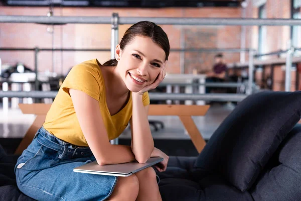 Glückliche Geschäftsfrau sitzt auf dem Sofa und hält Laptop, während sie in die Kamera schaut — Stockfoto