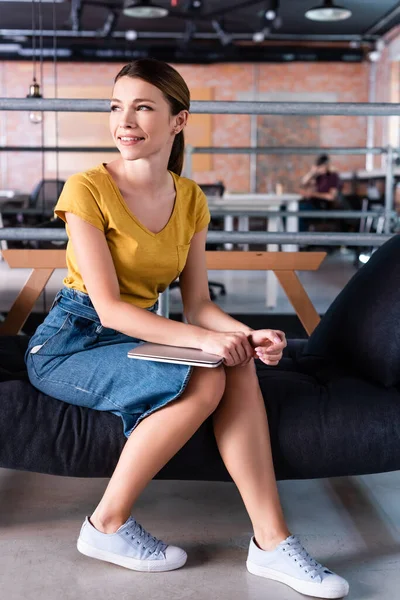 Happy businesswoman sitting on sofa and holding laptop in office — Stock Photo