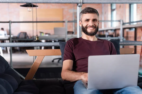 Веселий бізнесмен сидить на дивані і використовує ноутбук в офісі — стокове фото
