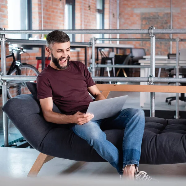 Aufgeregter Geschäftsmann sitzt auf Sofa und benutzt Laptop im Büro — Stockfoto