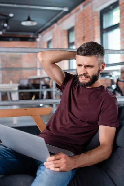 Displeased businessman sitting on sofa and using laptop in office — Stock Photo