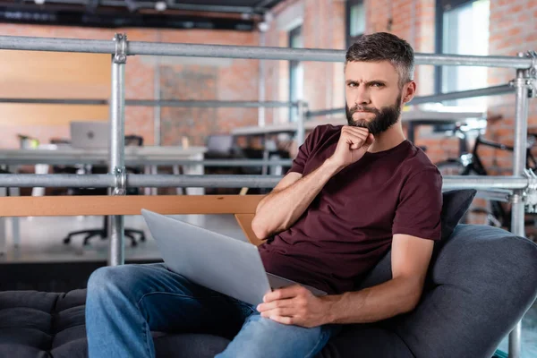 Cher homme d'affaires penser et toucher ordinateur portable tout en étant assis sur le canapé dans le bureau — Photo de stock