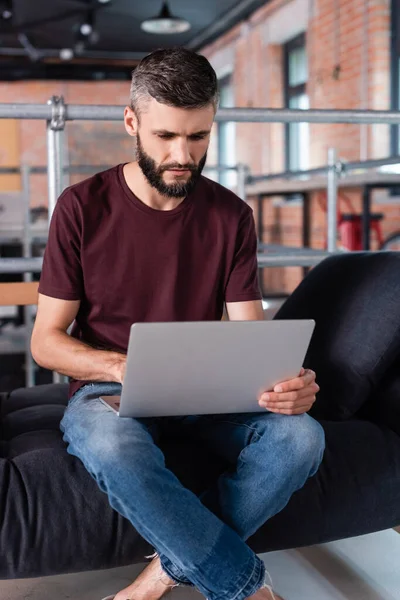 Schöner Geschäftsmann mit überkreuzten Beinen, der auf dem Sofa sitzt und Laptop im Büro benutzt — Stockfoto