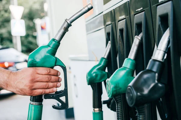 Cropped view of man holding fueling nozzle on gas station on urban street — Stock Photo