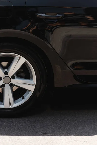 Wheel and door of black car on road with sunlight — Stock Photo