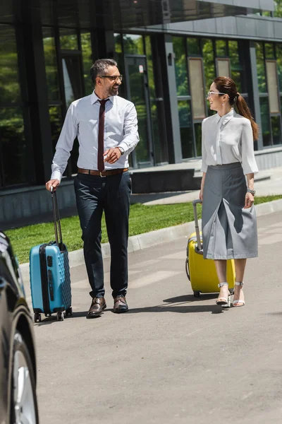 Selective focus of smiling business people walking with suitcases on urban street — Stock Photo