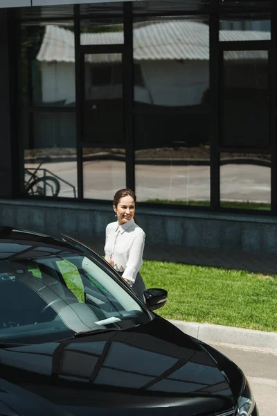 Smiling businesswoman holding eyeglasses near car on urban street — Stock Photo