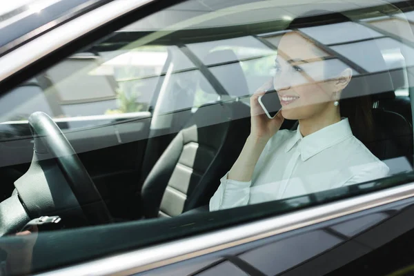 Selektiver Fokus einer Geschäftsfrau, die auf dem Fahrersitz im Auto mit dem Smartphone spricht und lächelt — Stockfoto