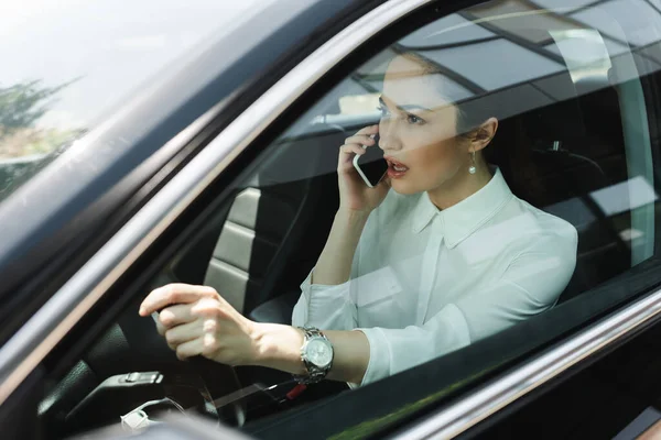Enfoque selectivo de la mujer de negocios hablando en el teléfono inteligente mientras conduce auto - foto de stock