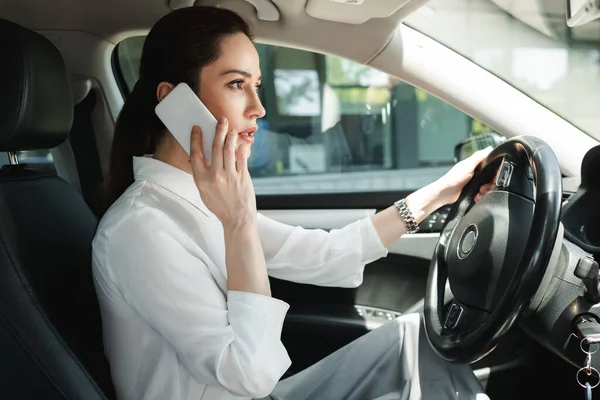 Vista lateral de la hermosa mujer de negocios hablando en el teléfono inteligente mientras conduce el coche - foto de stock