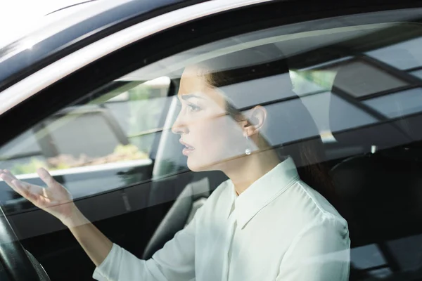 Foco seletivo de mulher de negócios confusa apontando com a mão enquanto dirige o carro — Fotografia de Stock