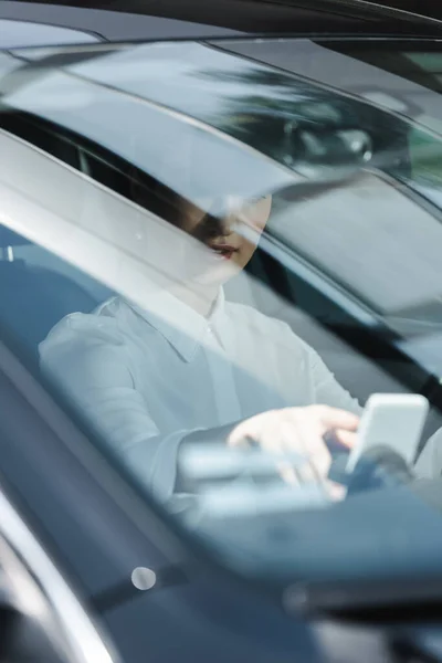 Selective focus of businesswoman using smartphone on driver seat in auto — Stock Photo