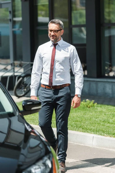 Selective focus of handsome businessman walking to car on urban street — Stock Photo