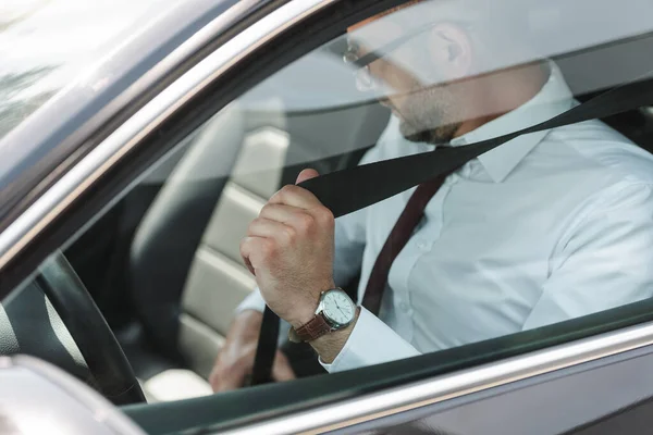 Selective focus of businessman fastening seat belt in car — Stock Photo