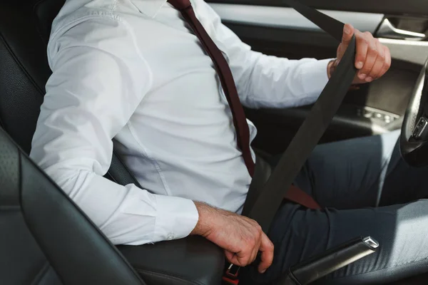 Vista recortada del hombre de negocios que sujeta el cinturón de seguridad en el asiento del conductor en el coche - foto de stock