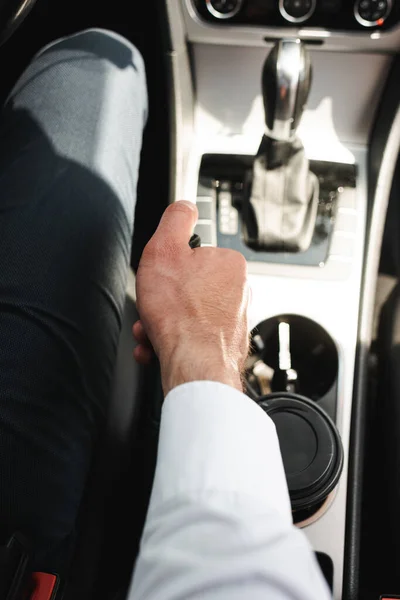 Vista recortada de un hombre de negocios conduciendo un coche cerca de la taza desechable en el portavasos - foto de stock