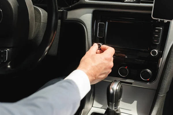 Vista recortada del hombre de negocios ajustando el sistema de audio del vehículo mientras conduce el coche - foto de stock