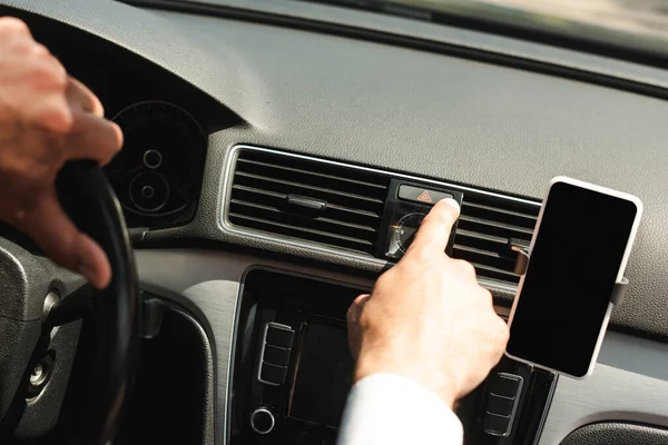 Cropped view of man turning on warning sign near smartphone while driving car — Stock Photo
