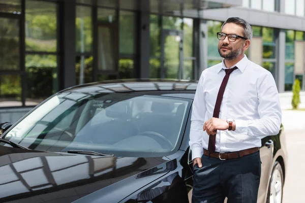 Handsome businessman with hand in pocket looking away near auto on urban street — Stock Photo