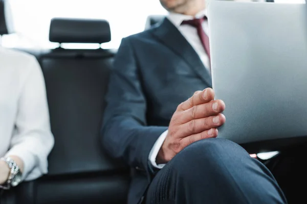 Cropped view of businessman holding laptop near businesswoman in car — Stock Photo