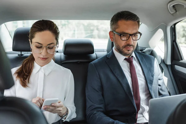 Concentration sélective des gens d'affaires utilisant des appareils numériques dans la voiture — Photo de stock