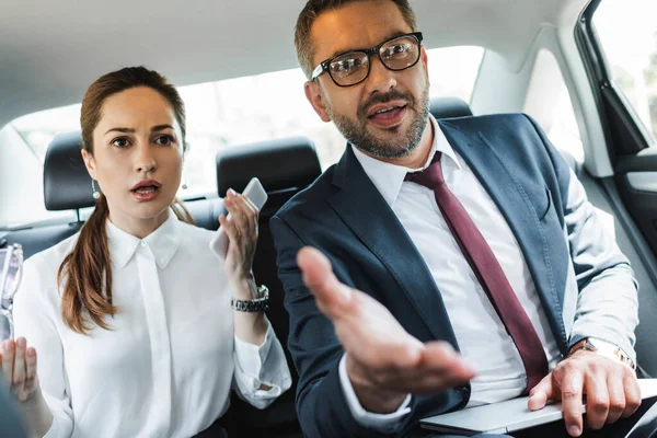 Selective focus of confused business people with gadgets looking away in car — Stock Photo