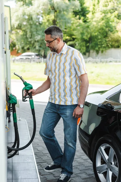 Foco seletivo do homem segurando o bico de abastecimento no posto de gasolina perto do automóvel na rua urbana — Fotografia de Stock