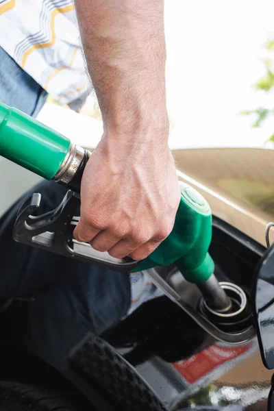 Cropped view of man holding fueling nozzle near open gas tank cover outdoors — Stock Photo