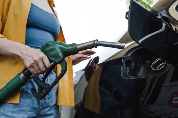 Vista ritagliata della donna che tiene l'ugello di rifornimento vicino all'auto sulla stazione di servizio — Foto stock