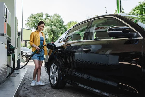 Schöne lächelnde Frau tankt Auto an Tankstelle — Stockfoto