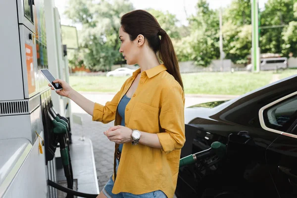 Frau hält Smartphone und Kreditkarte in der Nähe von Auto an Autotankstelle — Stockfoto