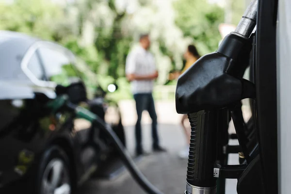 Enfoque selectivo de la boquilla de carga en la gasolinera y la pareja de pie cerca de auto al aire libre - foto de stock