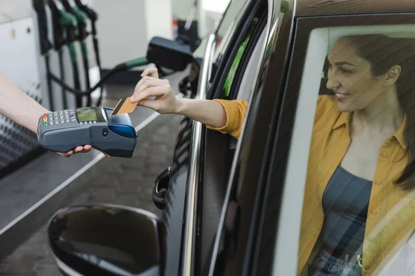 Selektiver Fokus des Tankstellenmitarbeiters mit Zahlungsterminal in der Nähe einer lächelnden Frau, die mit Kreditkarte im Auto bezahlt — Stockfoto