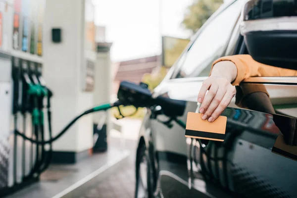 Enfoque selectivo de la mujer que sostiene la tarjeta de crédito mientras está sentado en el coche en la gasolinera - foto de stock