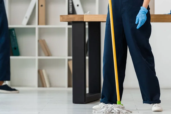 Vue recadrée du nettoyant dans le plancher de lavage en gant de caoutchouc avec serpillière dans le bureau — Photo de stock