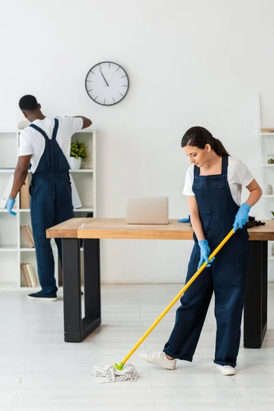 Multiethnic cleaners in uniform and rubber gloves cleaning office — Stock Photo