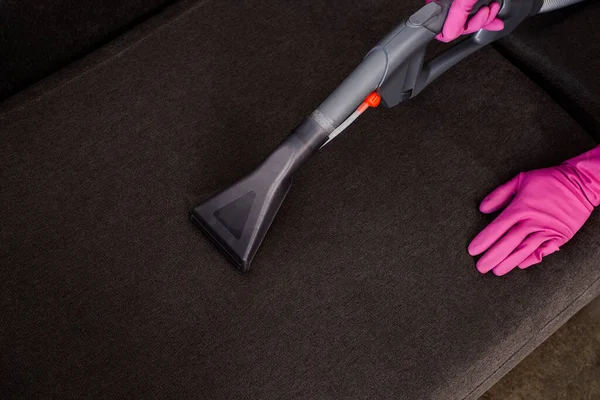 Vista recortada de la limpiadora en guantes de goma sofá de limpieza con aspiradora - foto de stock