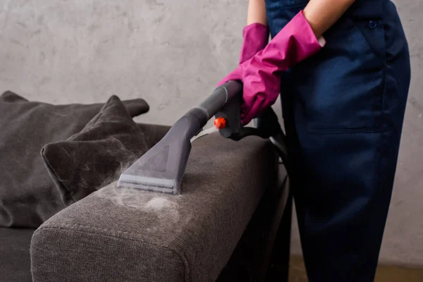 Cropped view of cleaner using vacuum cleaner with hot steam on couch upholstery — Stock Photo