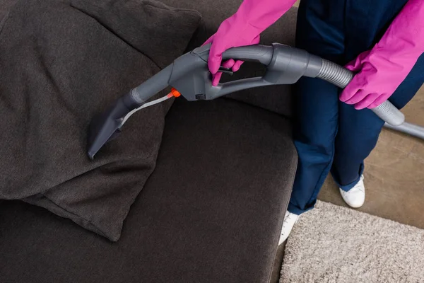 Ausgeschnittene Ansicht des Reinigers in Gummihandschuhen mit Staubsauger auf dem Kissen auf der Couch — Stockfoto