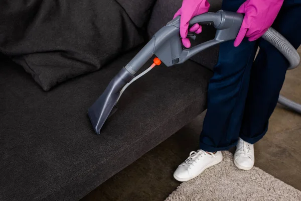 Обрізаний вид очищувача в гумових рукавичках, що тримає пилосос біля дивана — стокове фото