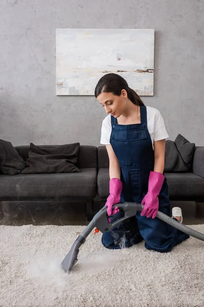 Привабливий прибиральник в уніформі і гумових рукавичках з використанням пилососа з гарячою парою в домашніх умовах — стокове фото