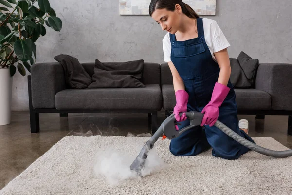 Schöne Reinigungsmittel in Gummihandschuhen Teppich mit heißem Dampf im Wohnzimmer reinigen — Stockfoto