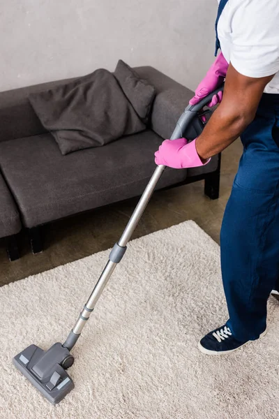 Vue recadrée du nettoyeur afro-américain en uniforme à l'aide d'un aspirateur à la maison — Photo de stock