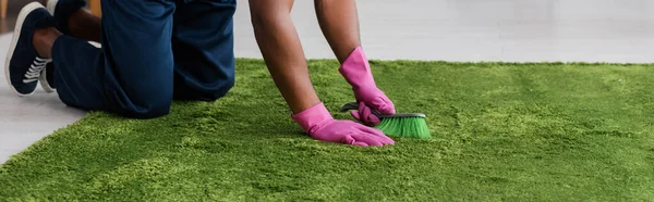 Panoramic crop of african american worker of carpet cleaning service using brush in living room — Stock Photo