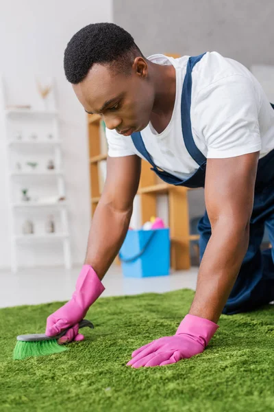 Selective focus of african american worker of carpet cleaning service using brush while working in office — Stock Photo