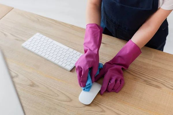 Cropped view of cleaner cleaning computer mouse with rag on office table — Stock Photo