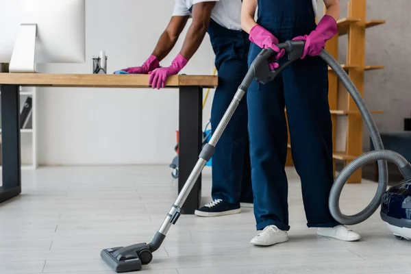 Cropped view of multiethnic cleaners using vacuum cleaner and rag in office — Stock Photo