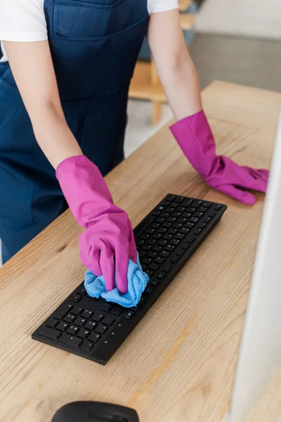 Vista recortada del trabajador del servicio de limpieza del teclado del ordenador con trapo en la mesa - foto de stock